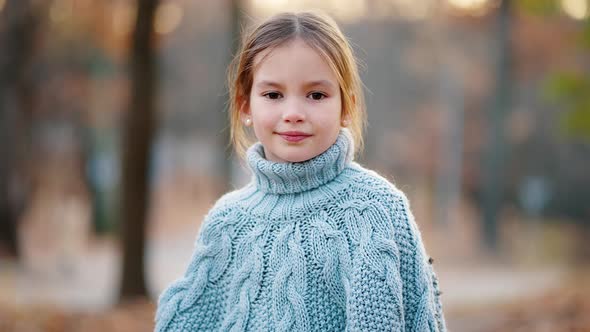 Little Blonde Girl is Looking at you and Smiling Posing Standing in Autumn Park