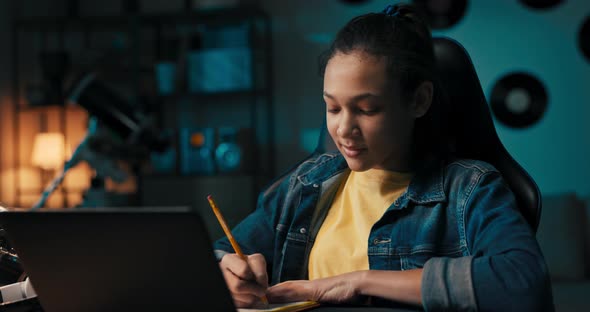 Girl Studies Diligently in Front of Laptop Notes with Pencil in Notebook Rewrites Reads Ebook Remote