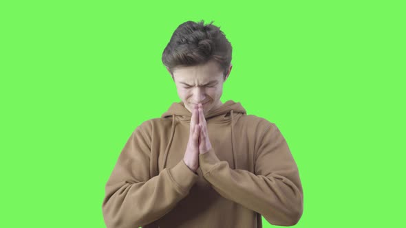 Desperate Boy Praying at Green Background. Portrait of Teenage Brunette Caucasian Believer with alt