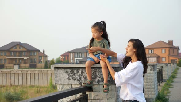 Careful Mother Holds Hand of Little Girl on City Embankment