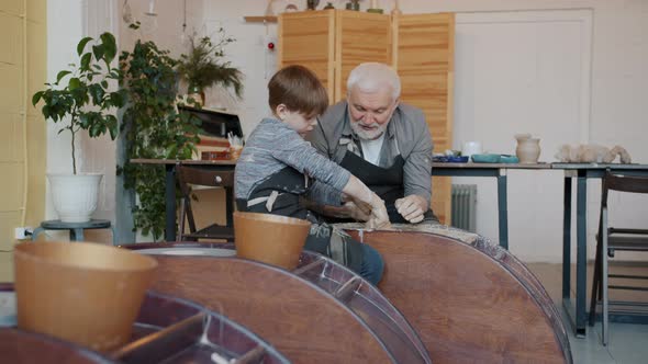 Grandfather Teaching Little Boy in Pottery Class Using Throwing-wheel Working with Clay