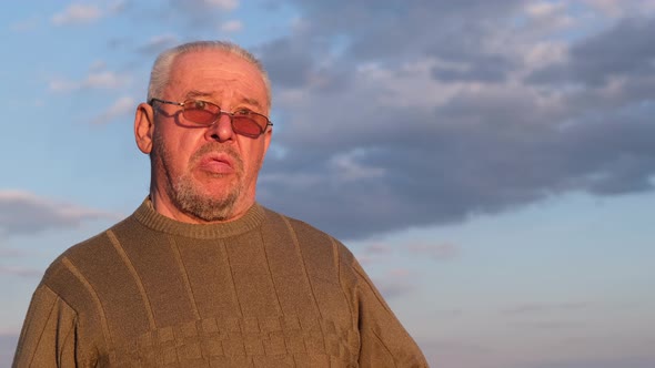 An Old Man in a Gray Sweater and Sunglasses Against a Blue Sky