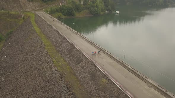 Aerial view of three bicyclist biking over the dam in Colibita Lake, Romania, during Tura Cu Copaci