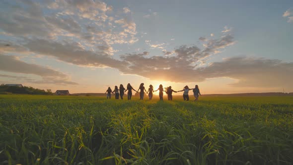 Eleven Cheerful Girls Run to the Meeting Across the Field in the Summer Holding Hands