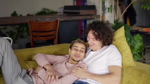 Young Gay Male Couple Relax on Couch Embracing Having Fun