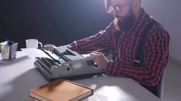 Writer's Day Concept. Young Male Writer in a Dark Room Typing on a Typewriter
