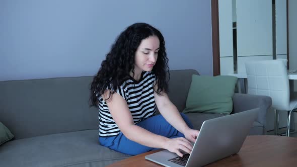 Young Serious Woman Working on Laptop, Sitting on Sofa at Home, Businesswoman Sits at Home Works