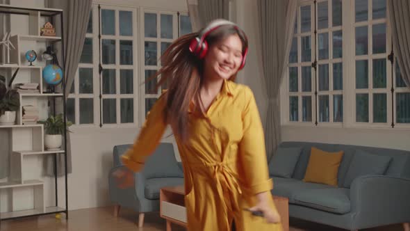 Funny Young Asian Lady Hold Sing Telephone, Wear Headphones And Dancing In Living Room