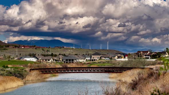 Time Lapse of wind turbines turning on a beautiful cloudy day in suburban setting with a river and b