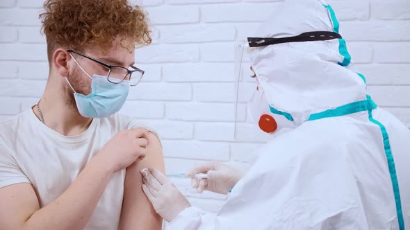 Doctor in Protective Suit and Mask Making Injection From Covid19 for Young Man