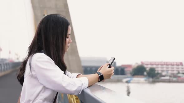 Asian woman using smartphone chatting with friends and browsing social media on a mobile phone.