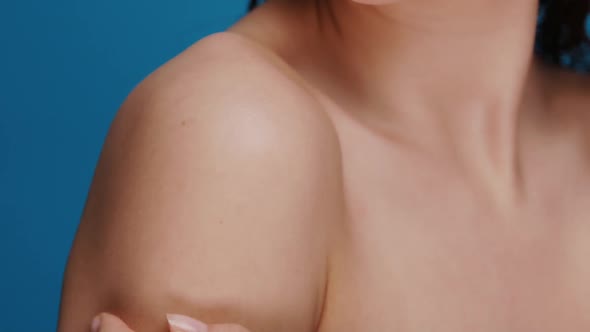 Close-up of Female Arm Moisturizing and Massaging Her Shoulder on Blue Background