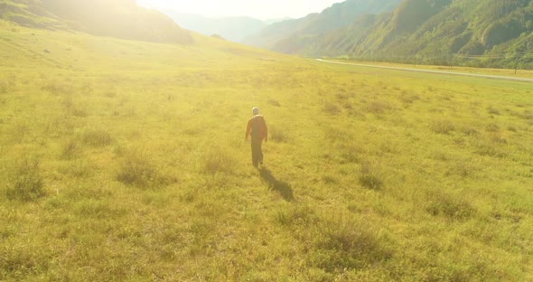 Flight Over Backpack Hiking Tourist Walking Across Green Mountain Field. Huge Rural Valley at Summer