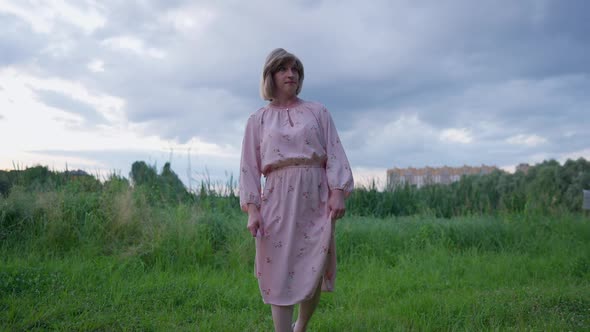 Portrait of Frustrated Depressed Transgender Woman in Pink Dress Walking in Slow Motion on Green