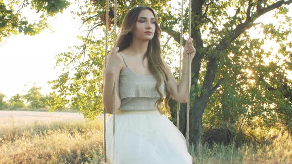 young happy woman swaying rope swing on oak tree,summer leisure at sunset, healthy lifestyle