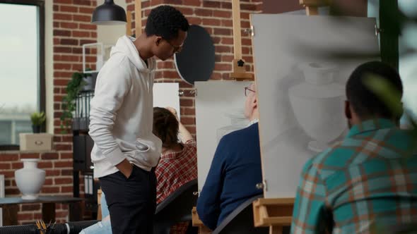 Young Man Looking at Elder Student Drawing Vase Model