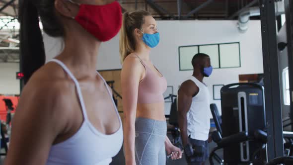 Diverse fit people wearing face masks exercising using dumbbell in the gym