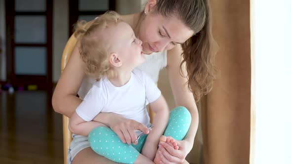 mother cuts toenails to her little daughter. Mom and baby spend time together