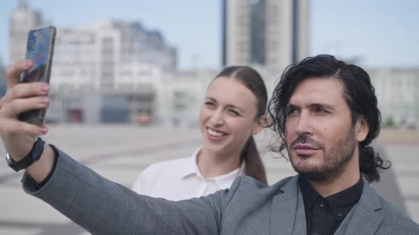 Cheerful Elegant Man and Woman Taking Selfie Standing Downtown on City Square