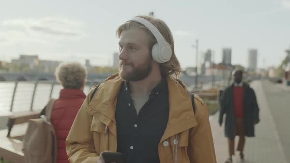 Man Walking in City and Listening to Music with Headphones