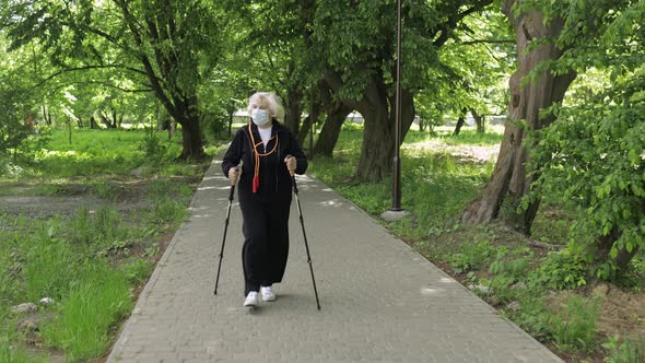 Active Senior Old Woman in Mask Training Nordic Walking in Park at Quarantine