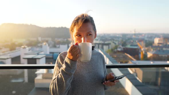 Woman Starts Her Day with a Cup of Tea or Coffee and Checking Emails in Her Smartphone on the