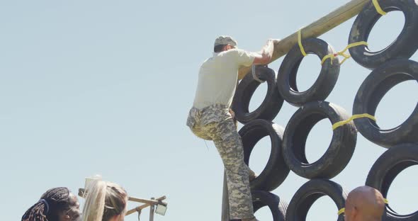 Fit caucasian male soldier in combat uniform climbing tyre wall on army obstacle course in the sun