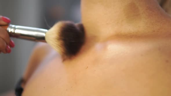 Closeup View of a Brush Applying Golden Powder on the Model's Neck and Chest