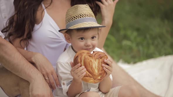 A Little Caucasian Boy with Pretty Face Eats an Yummy Bun in the Park