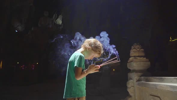 Slowmotion Shot of a Little Boy Which Is Praying Holding Smoking Aroma Sticks in His Hands. He Is in