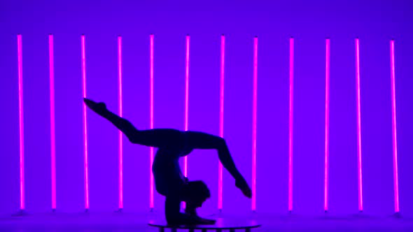 Athlete Performs Gymnastics in the Studio Against the Backdrop of Colorful Neon Lights