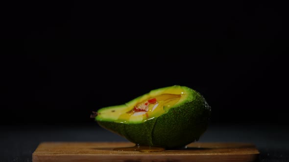 Olive Oil Spreading on Green Avocado in Slow Motion at Black Background