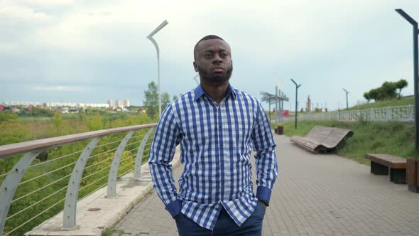 Young Afro American Man is Walking in City Park in Cloudy Summer Day