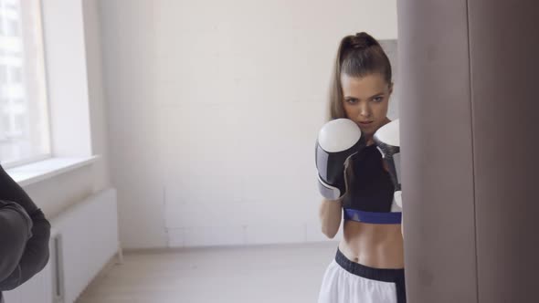 A Strict Trainer Watches His Female Kickboxer Student Practice a Punch on a Punching Bag in a