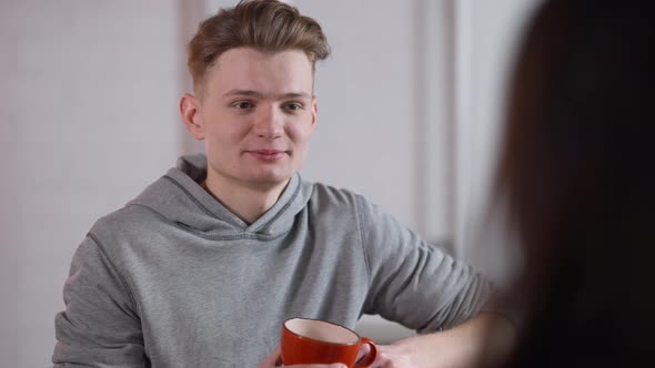 Portrait of Young Happy Loving Man Talking with Woman and Drinking Coffee in Cafeteria
