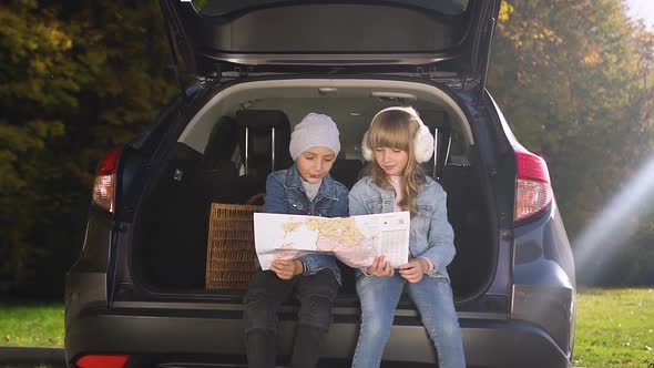 Teen Modern Boy and Girl Sitting in the Trunk and Using Roadmap to Planning their Joint Trip
