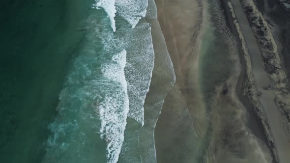 Flying over the ocean (Norway) looking down at the waves and the beach. Tilt up of the camera to foc