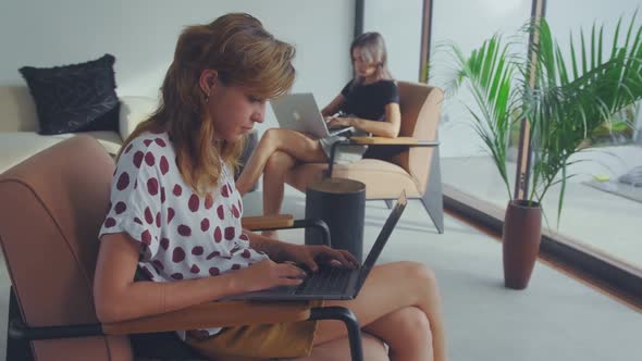 Two Female Coworkers Maintaining Social Distancing While Working on Laptops