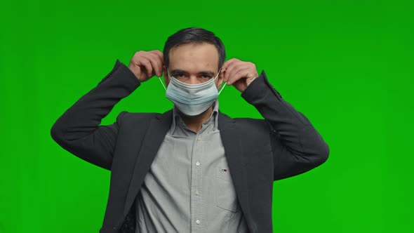 Man Putting on Face Medical Mask Against Virus Prevention Outbreak on Green Background