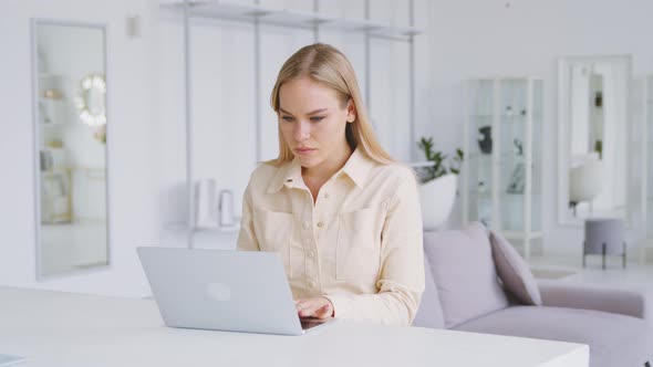 Thinking girl at the desk with a laptop in a white room. Portrait of young woman