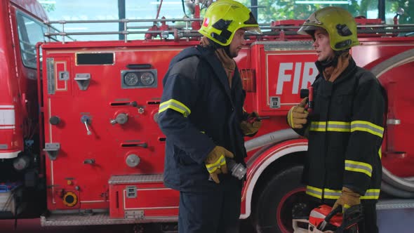 Two fireman hold tools and discuss together for preparation of firefighting