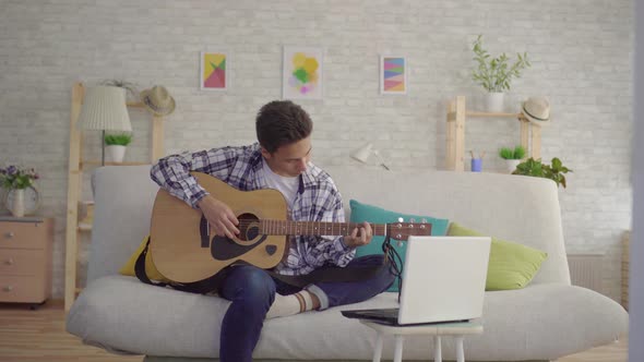 a Young Asian Man Learns To Play the Guitar Depends on the Laptop Training Video