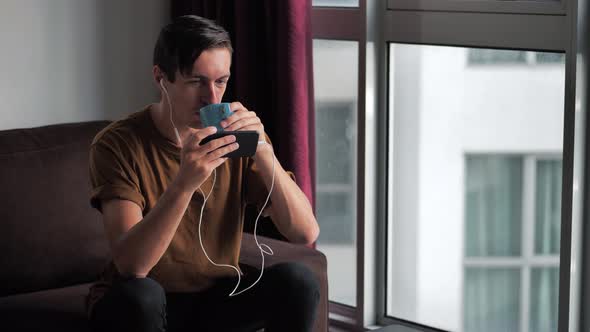 Smiling Man in Headphones Enjoys a Smartphone Watching Media in Social Networks While Sitting at