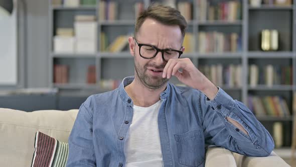 Portrait of Upset Young Man Sitting on Sofa and Crying 