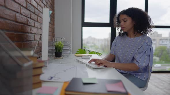 Side View of Serious African American Young Woman Typing on Keyboard and Moving Computer Mouse in