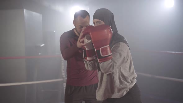 Coach Correcting Boxing Stance of Young Beautiful Muslim Woman in Hijab Training in Haze in