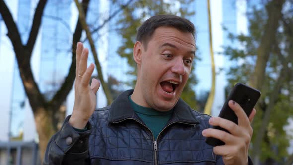 Excited Guy Looks at Phone and Celebrates Big Win Financial Good News Success Achievement Cell Phone