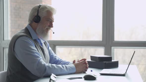 An Elderly Businessman in a Headset Having a Video Conference with a Business Partner Working in an