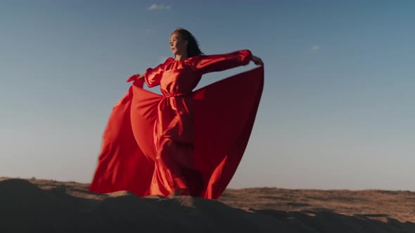 An Asian woman in a red dress whirls on sand dunes