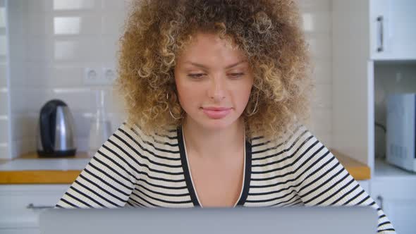 Beautiful curly woman working freelance at home on lockdown. Cute white female reading on computer